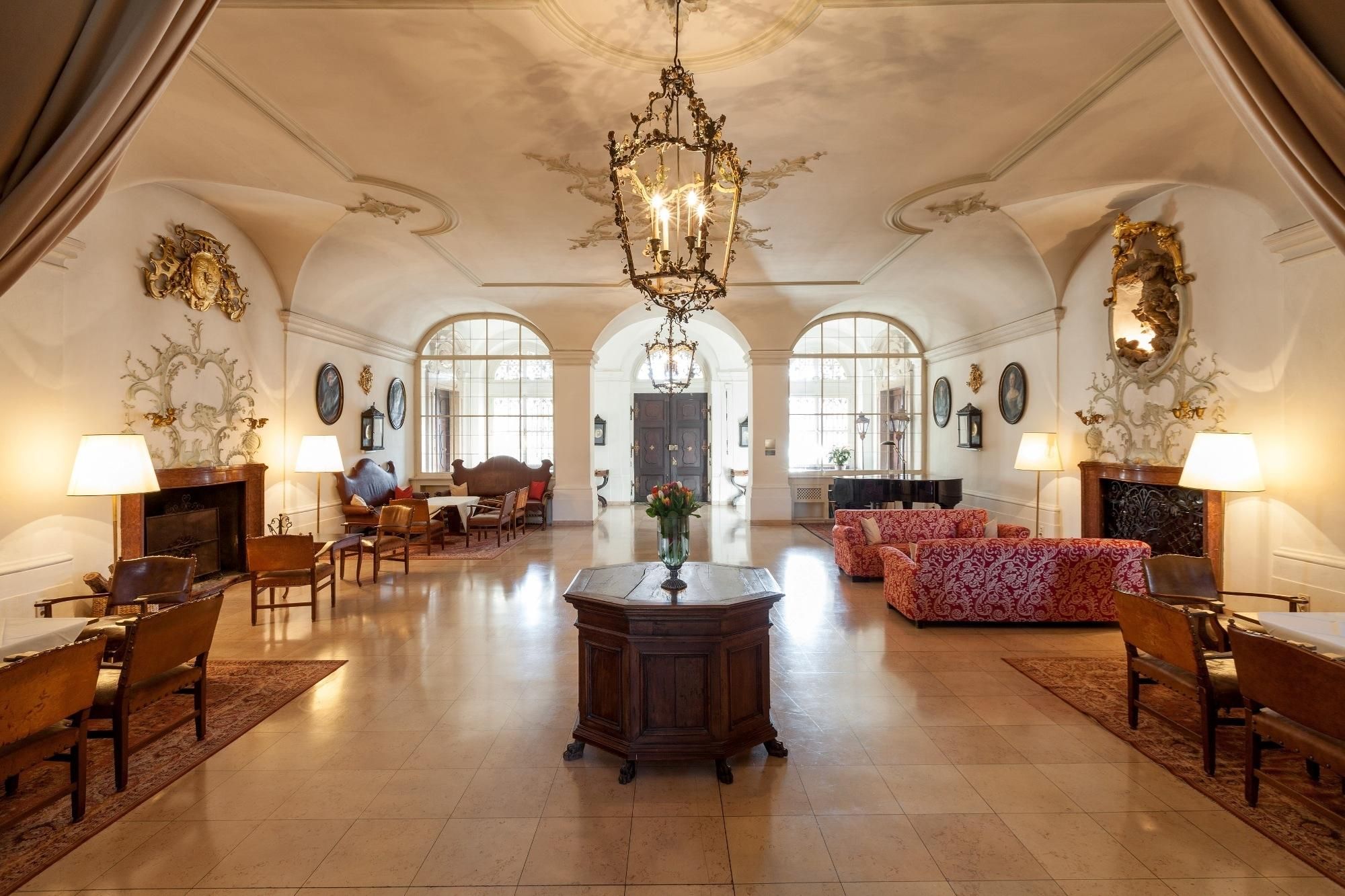 A spacious lobby with a grand chandelier, elegant furniture, and arched windows.