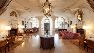 A spacious lobby with a grand chandelier, elegant furniture, and arched windows.