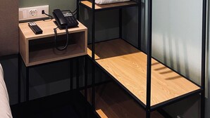 A compact room with a wooden wardrobe, a bedside table with a phone and remote, and a towel on the floor. - Albufeira Lounge Hotel (Albufeira)
