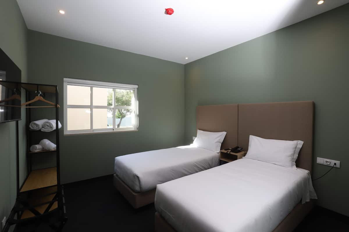 A room with two beds, a window, a shelf with towels, and a red ceiling light.