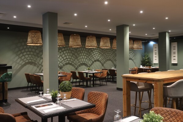 A restaurant with high tables and cushioned chairs, a patterned wall, and hanging lamps.