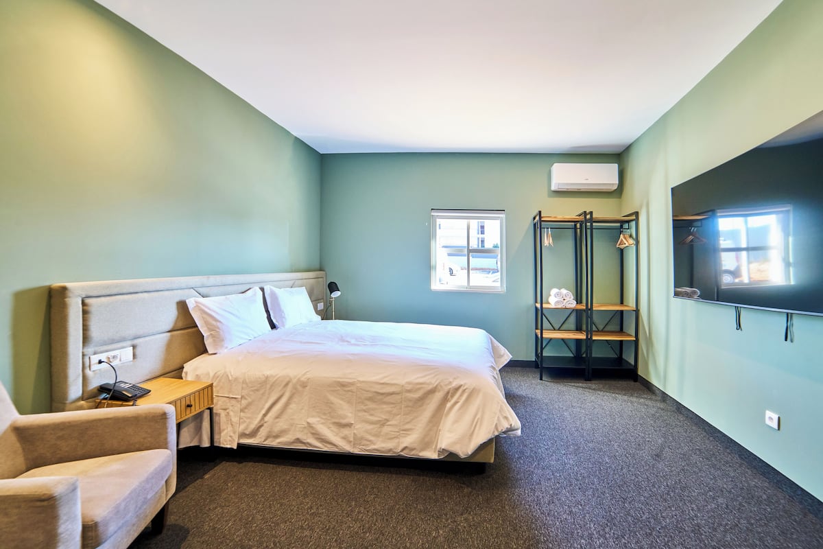 A hotel room with a bed, a chair, a wardrobe, and a TV.