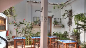 An outdoor patio with tiled flooring, wooden tables and chairs, and potted plants.