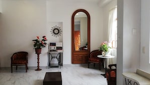 A room with a wooden door, a potted plant, a small table, a mirror, and a clock on the wall.