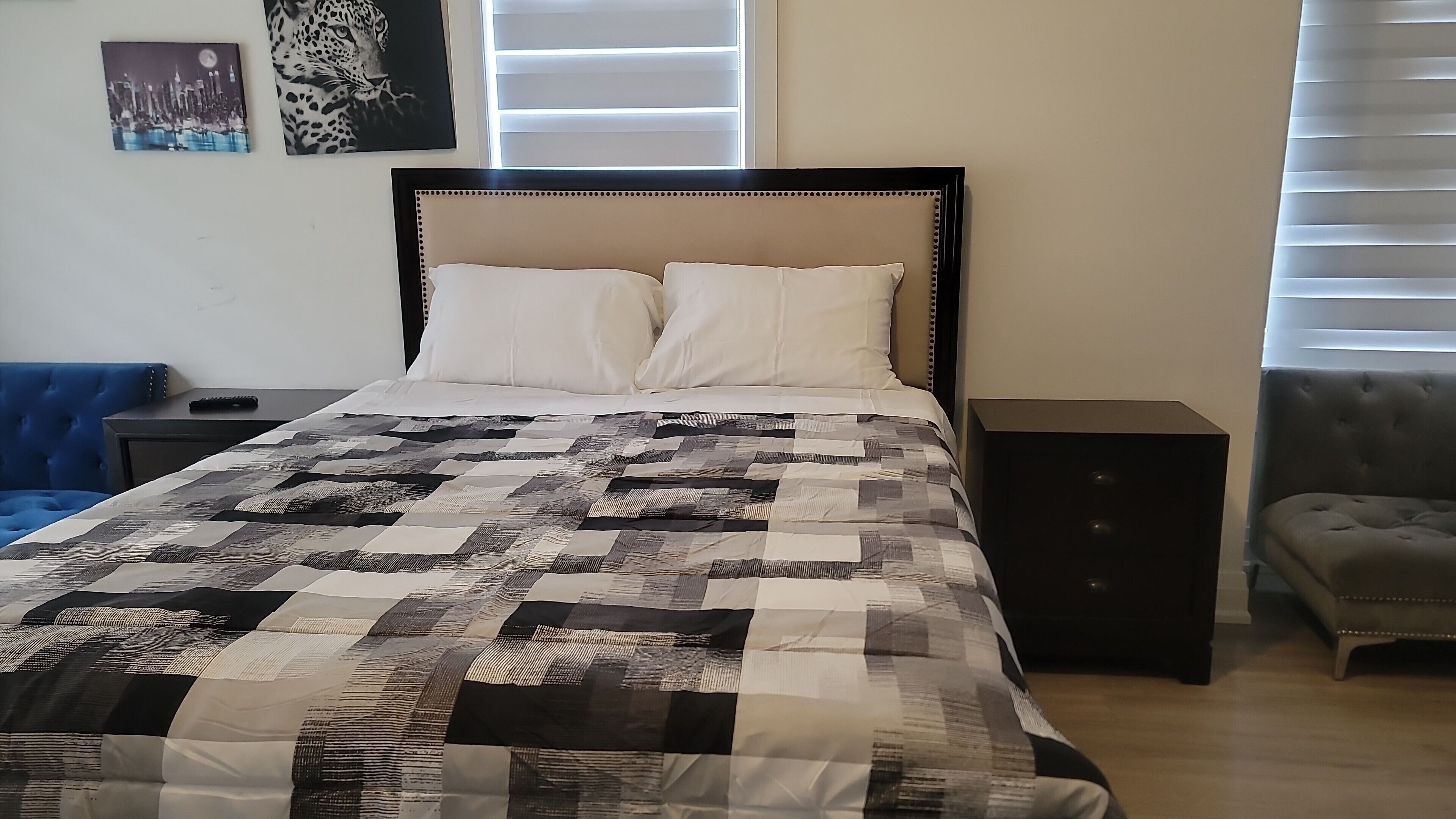 Uma cama bem arrumada com colcha, um criado-mudo, uma cadeira azul e uma mesa pequena.