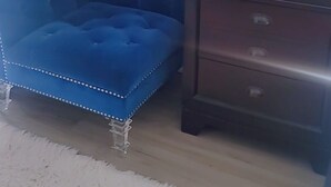 A corner room with a blue tufted chair, a small wooden nightstand with drawers, a potted plant, and a framed picture on the wall. - Modern Suite Near Hamilton Airport (Hamilton)