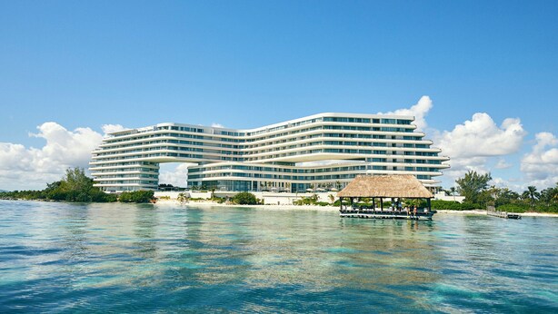 A large, multi-story hotel with a modern design, situated by a clear blue sea. - SHA Mexico - Lifestyle Optimization Program - Personalized Meal Plan (Cancun)