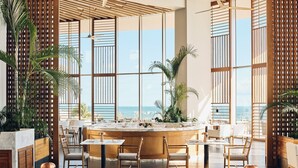 A modern dining area with a central island, seating around it, and large windows offering a view of the ocean. - SHA Mexico - Lifestyle Optimization Program - Personalized Meal Plan (Cancun)