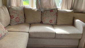 Een beige modulaire bank met kussens met een bloemenprint, geplaatst in een kamer met grote ramen en dunne gordijnen.