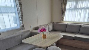 Een moderne woonkamer met een grijze bank, een houten salontafel en een vaas met bloemen.