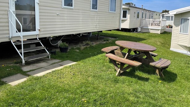 Een stacaravan met een terras, inclusief een picknicktafel en een trap naar de ingang.