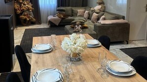 Un salon moderne avec un coin repas. La pièce est aménagée avec un ensemble de canapés, une grande sculpture d’ours en peluche et une table à manger, ainsi que des assiettes et des verres.