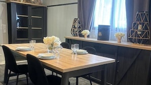 Un coin repas avec une table en bois dressée pour quatre personnes, des chaises noires et un tapis à motifs sombres.