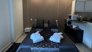A modern hotel room with a large bed, a small bedside table, a built-in desk with a chair, a microwave, and a black rug. - Bentley - Studio noire (Sanary-sur-Mer)