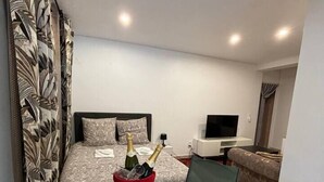 Un dormitorio con cama, mesita de noche, televisor y una pequeña zona de estar con mesa y sillas.