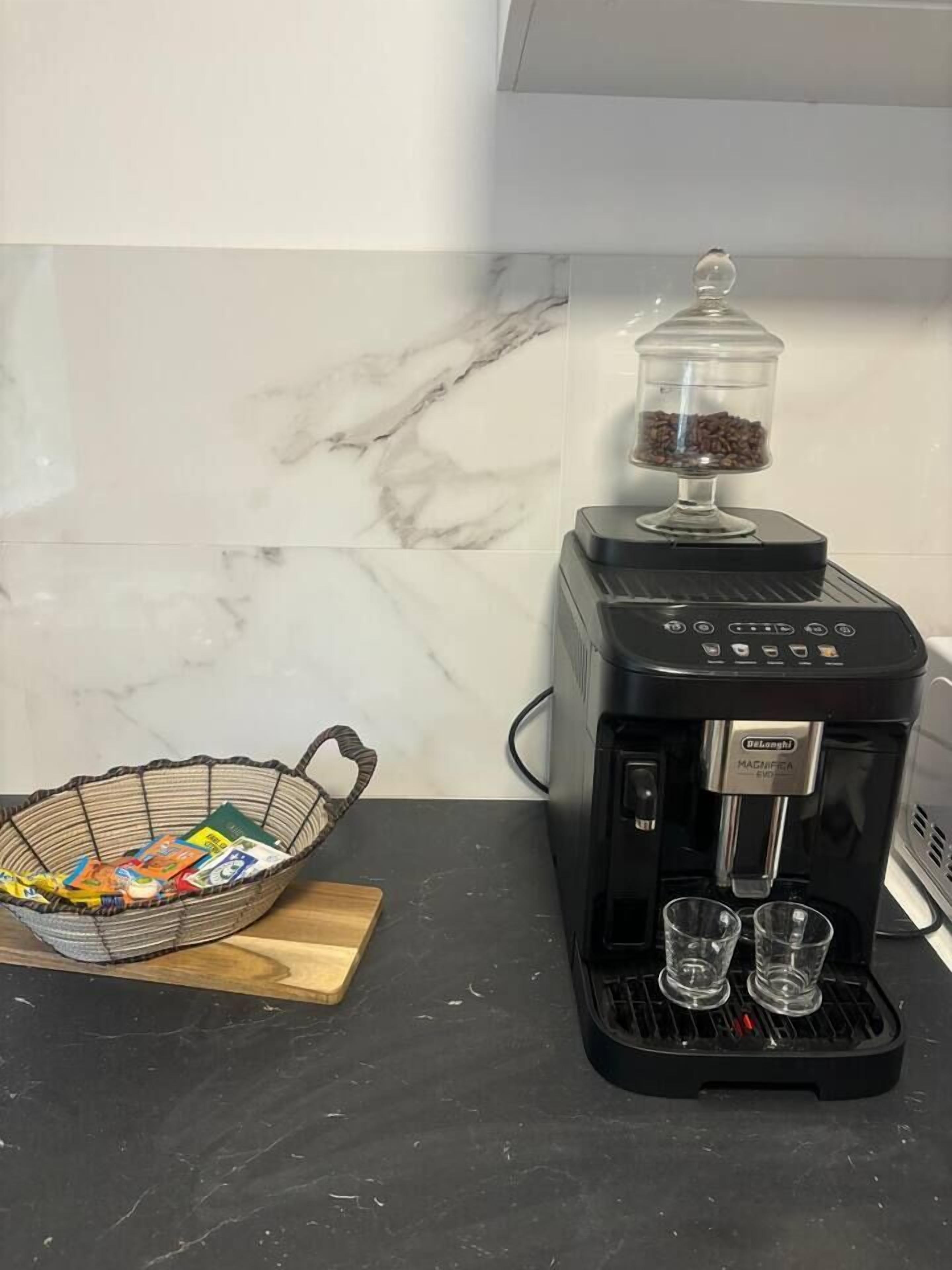 A coffee maker with a glass container on top, a basket with coffee pods, and two glasses on the counter.