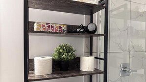 A bathroom with a wooden shelf holding toilet paper, a potted plant, and a decorative box. - Suite Near WEM: Game Room & Kitchen (Edmonton)
