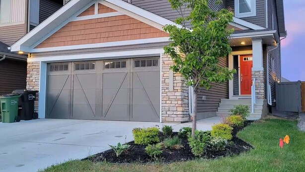 A two-story house with a garage, a small tree in the front yard, and a red door. - Suite Near WEM: Game Room & Kitchen (Edmonton)