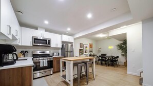 A modern kitchen with stainless steel appliances, a wooden island, and a dining area with a table and chairs. - Suite Near WEM: Game Room & Kitchen (Edmonton)