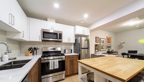 A modern kitchen with white cabinets, stainless steel appliances, a wooden dining table, and a tiled backsplash.