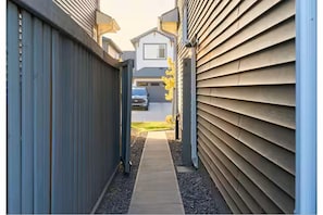 A narrow pathway leading to a residential building with a garage and a parked car.