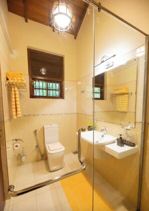 A bathroom with a glass shower enclosure, a toilet, a sink, and a window with blinds. - petit paradis hiriketiya (Dodampahala)