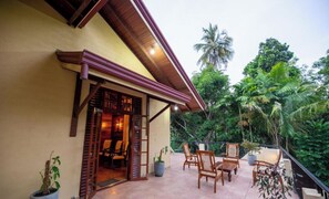 A traditional wooden building with a balcony, furnished with chairs and a table, surrounded by lush greenery. - petit paradis hiriketiya (Dodampahala)