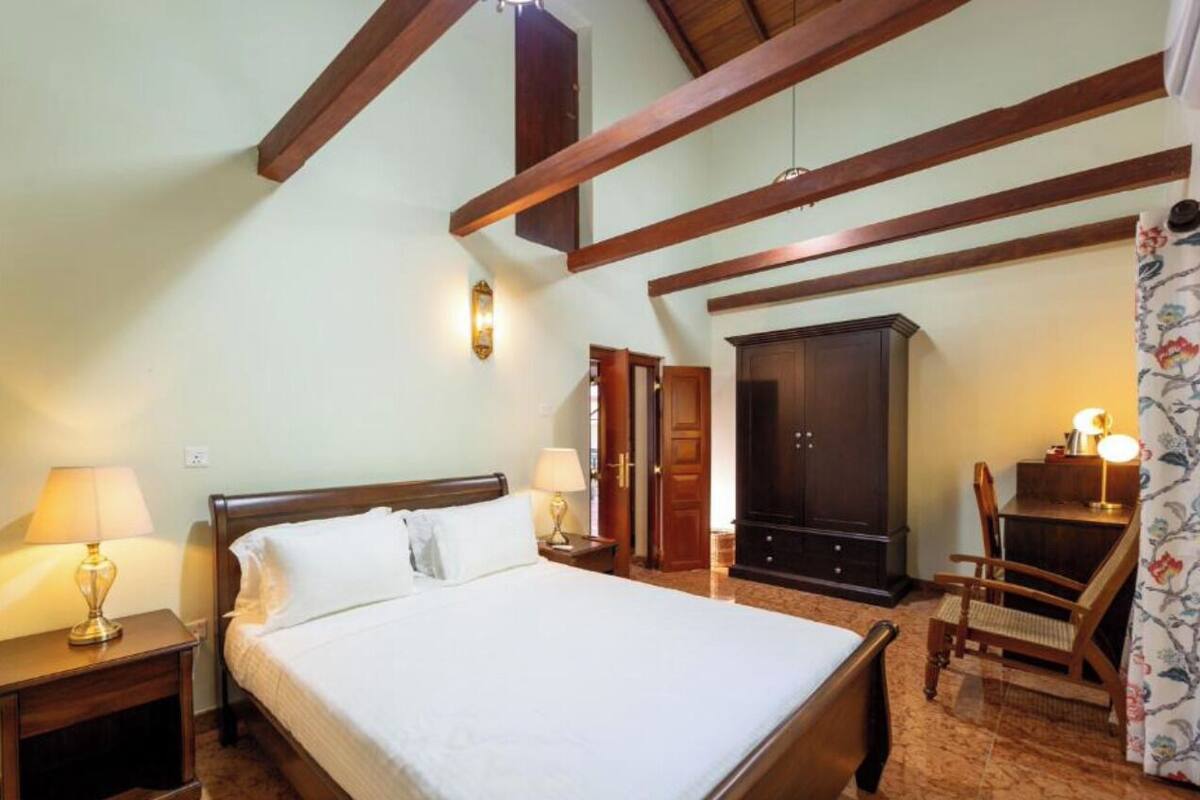 Une chambre avec un grand lit, des poutres en bois, une armoire, un bureau et une chaise.