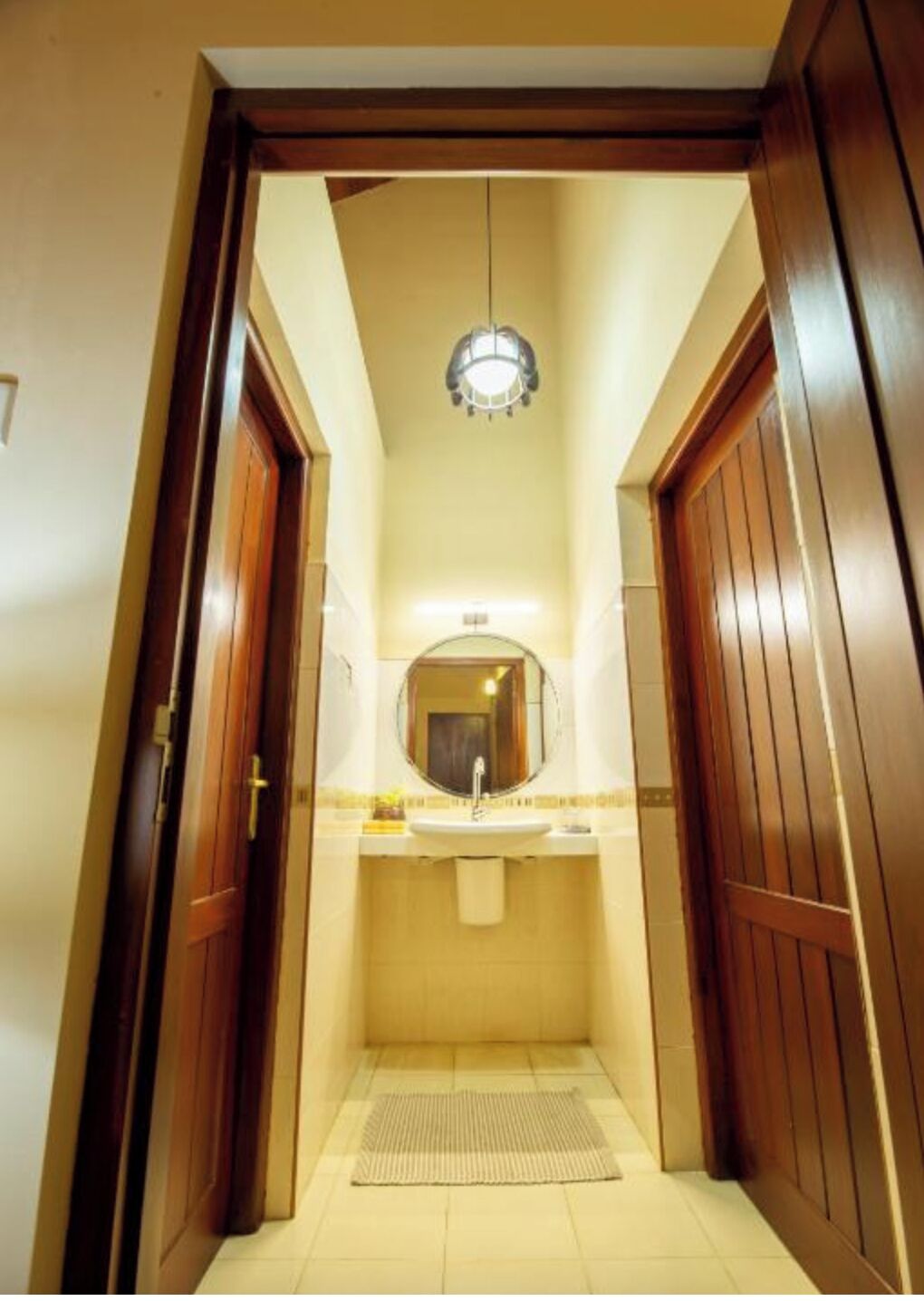 A narrow bathroom with a sink, mirror, and wooden doors.