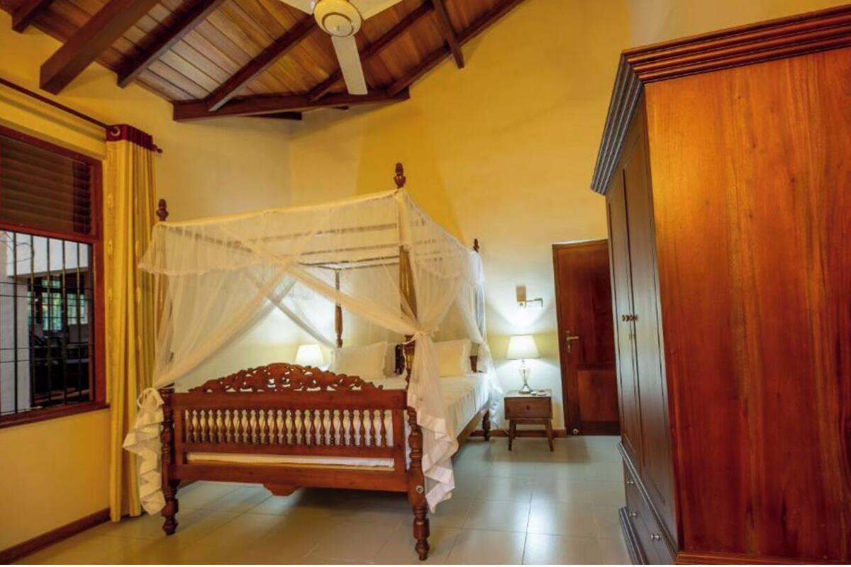 Une chambre à coucher avec un lit à baldaquin, une armoire en bois et un ventilateur de plafond.