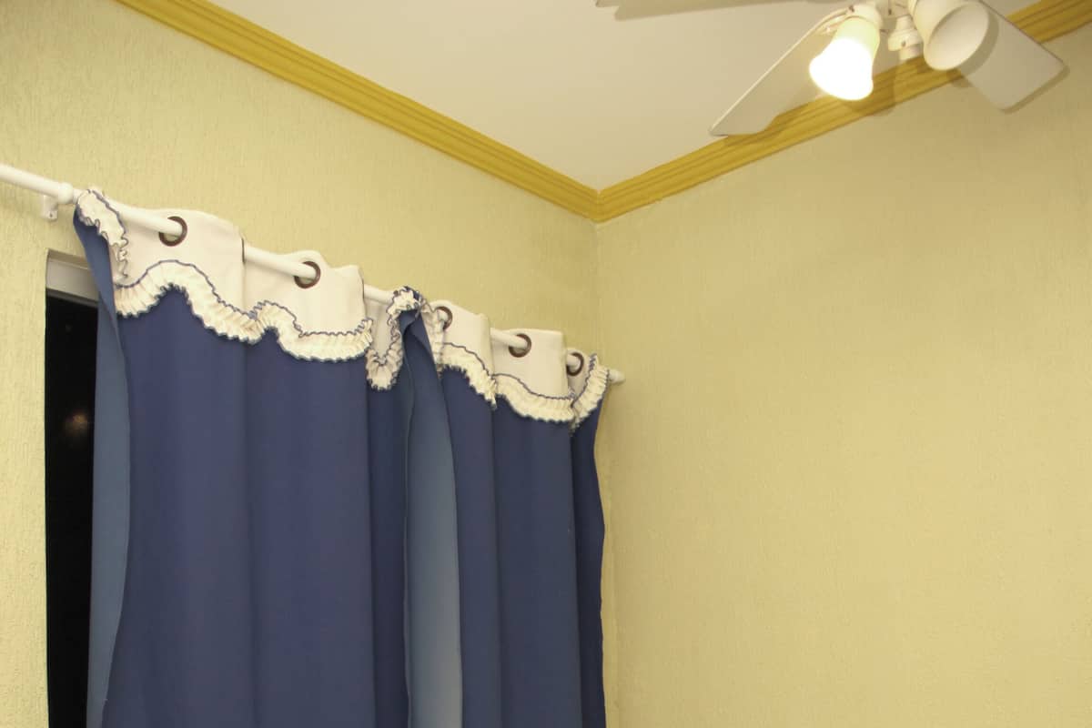 Une chambre d’hôtel avec un lit, du linge de lit blanc, une table de chevet, une lampe et un ventilateur de plafond.