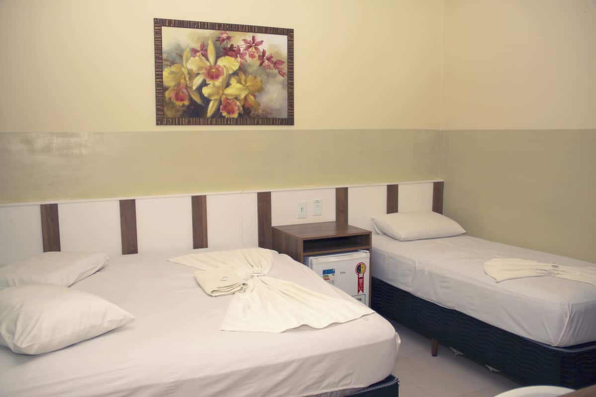Une chambre d’hôtel avec deux lits, une petite table, un réfrigérateur et un tableau au mur.