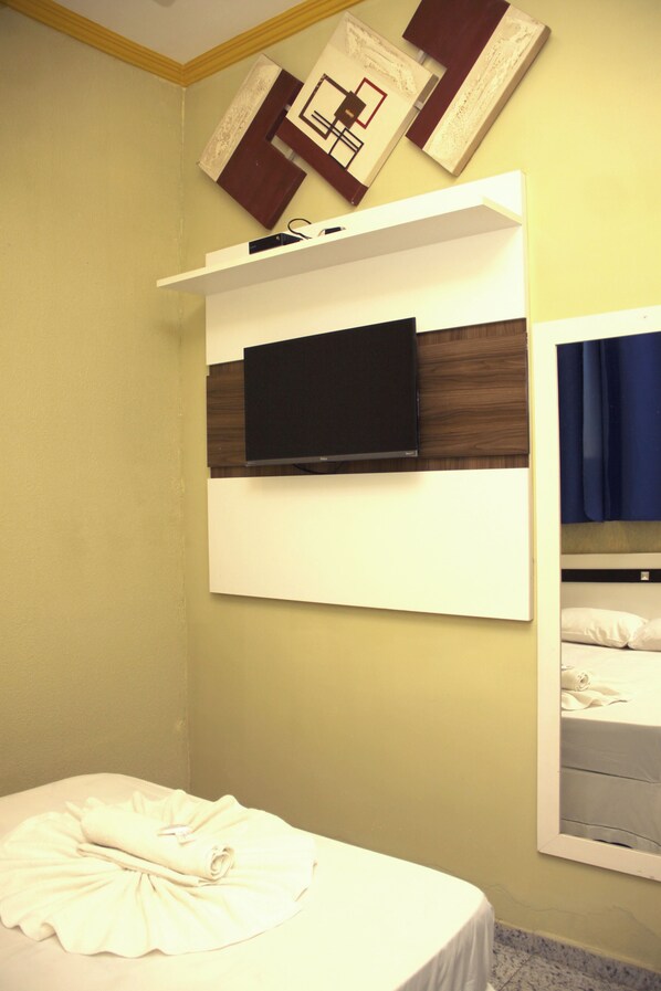 Ein Hotelzimmer mit einem Bett, einem an der Wand befestigten Fernseher und einem Regal über dem Bett.