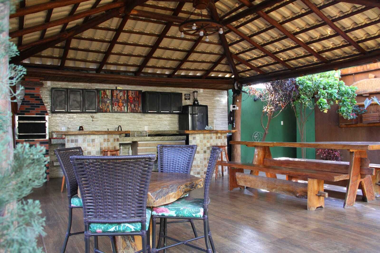 An outdoor dining area with wicker chairs and wooden tables, a brick oven, and a green wall with hanging plants.