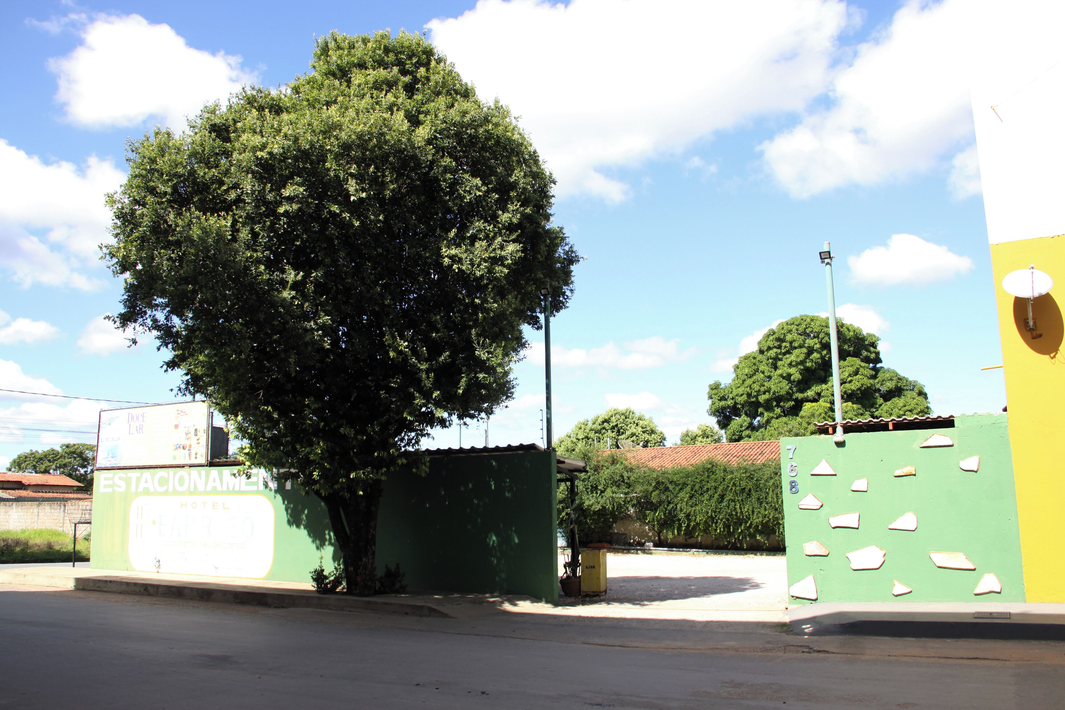 Um edifício verde com uma placa indicando 'Estacionamiento' e uma grande árvore em frente.