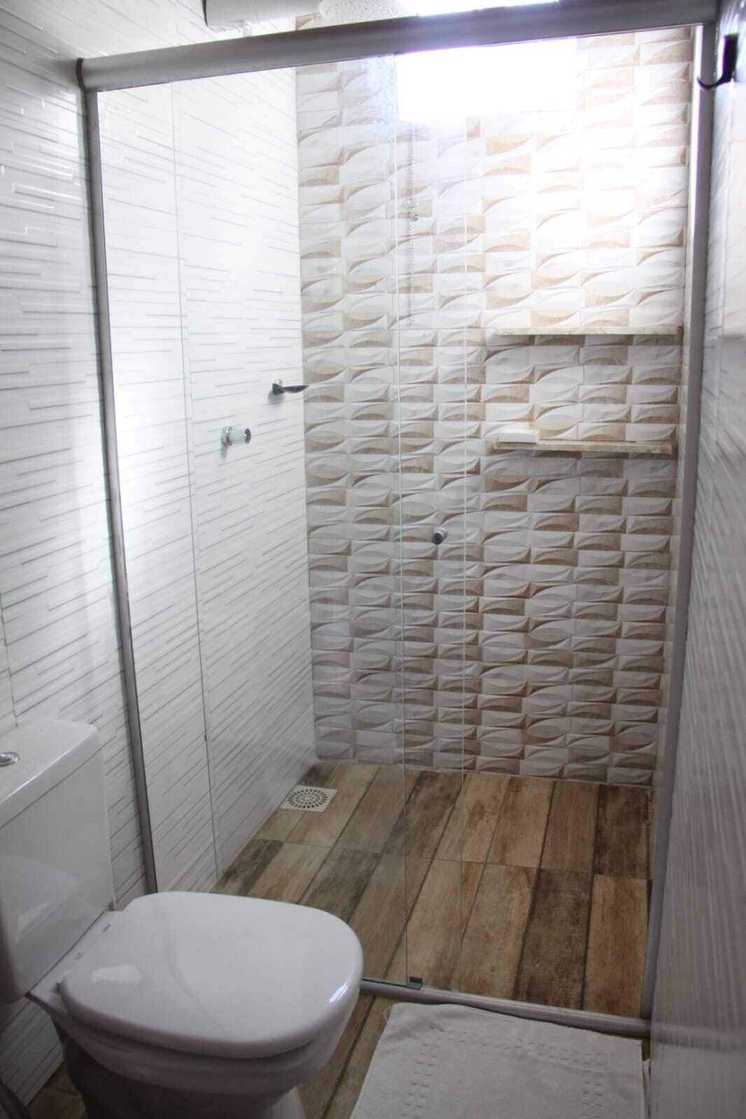 A bathroom with a white toilet, a shower with a textured wall, and a wooden floor.