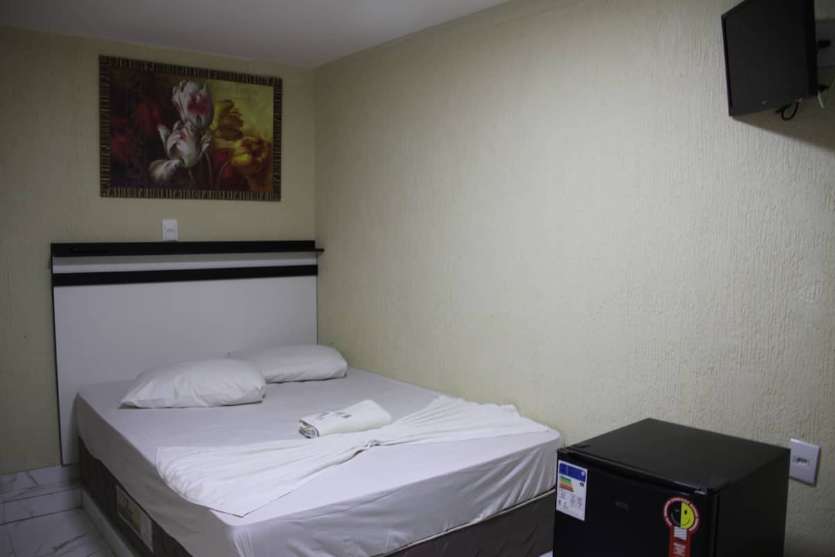 Une chambre d’hôtel avec un lit, un tableau au mur et un boîtier noir posé sur le sol.