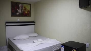 Una habitación de hotel con una cama, un cuadro en la pared y una caja negra en el suelo.
