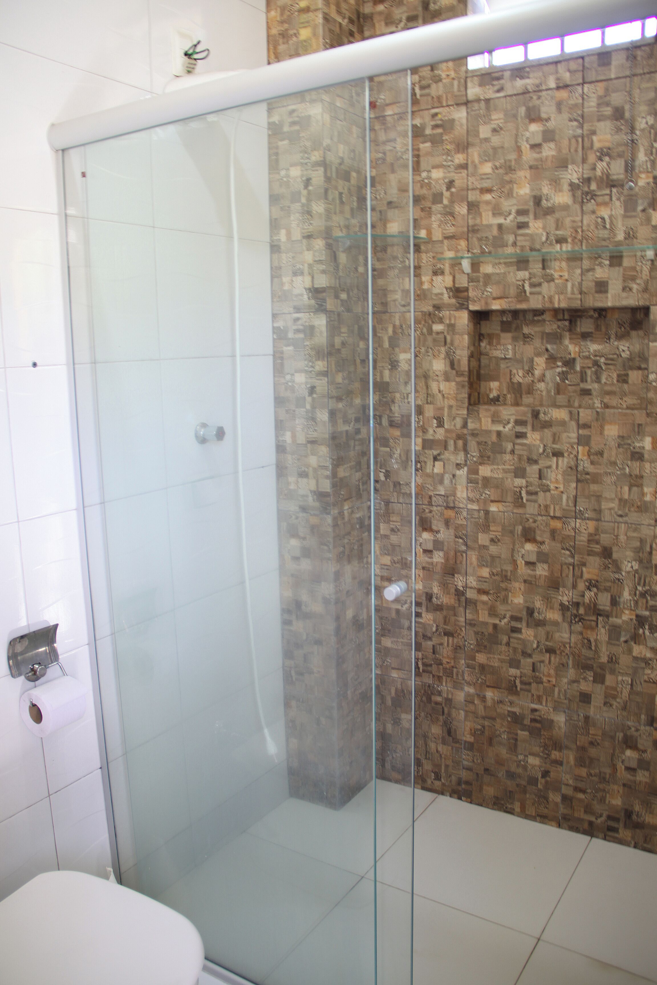 Eine Duschkabine aus Glas mit gefliestem Boden und einer Wand aus Mosaiksteinen.
