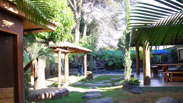 A garden with a wooden pergola, a small waterfall, and a dining area with tables and chairs. - Hotel Barroso (Pirapora)