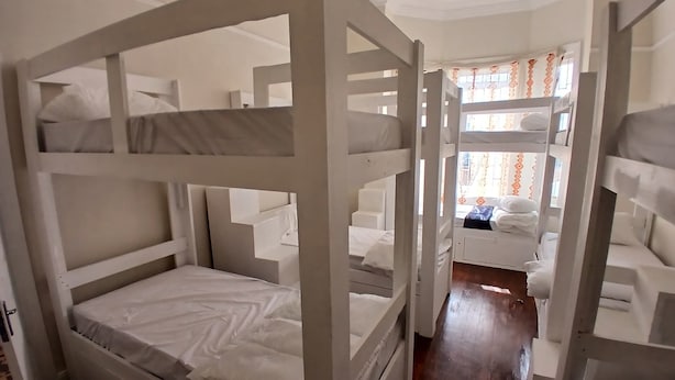 A room with bunk beds, wooden flooring, and a window with curtains. - V & A Backpackers (Western Cape)