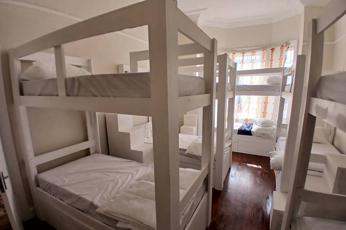A room with bunk beds, wooden flooring, and a window with curtains.
