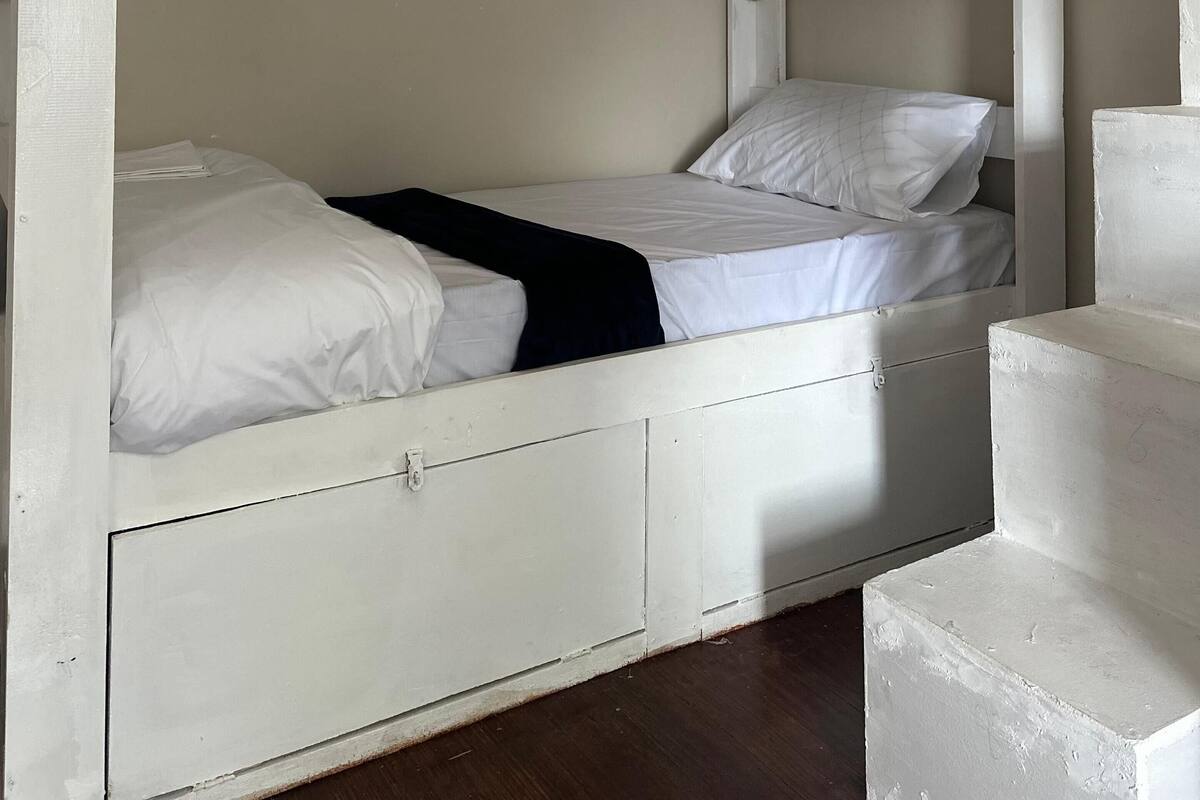A bunk bed with a lower bunk and a single bed, both with white bedding. There is a small drawer under the lower bunk.