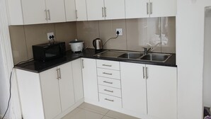 A modern kitchen with white cabinets, a black countertop, a microwave, a slow cooker, and a sink. - V & A Backpackers (Western Cape)