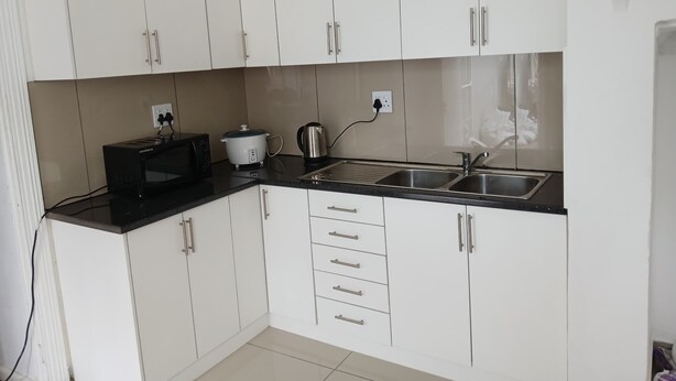 A modern kitchen with white cabinets, a black countertop, a microwave, a slow cooker, and a sink. - V & A Backpackers (Western Cape)