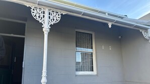 A building with a grey exterior, a white decorative column, and a window with metal bars. - V & A Backpackers (Western Cape)