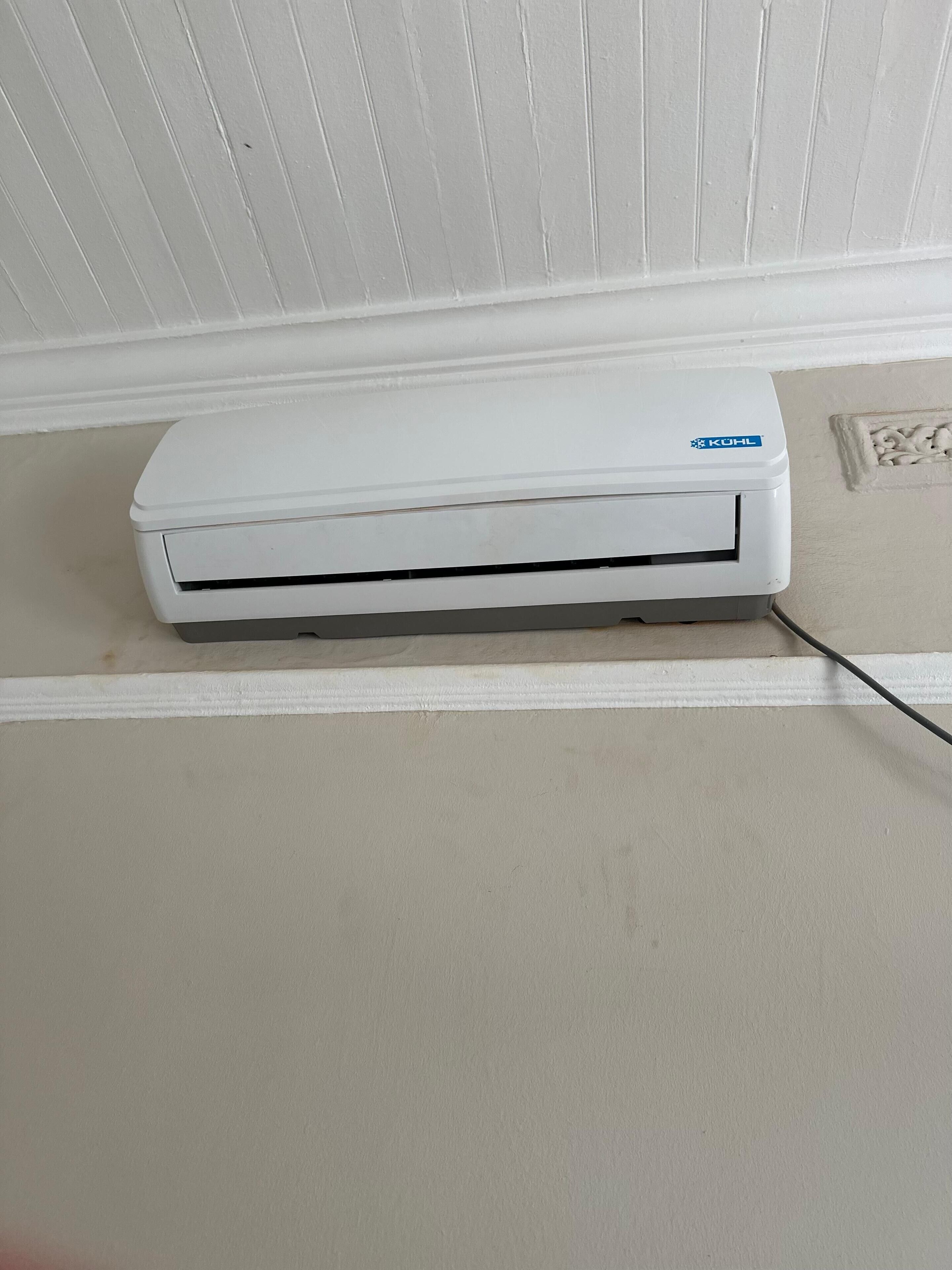 Un equipo de aire acondicionado blanco montado en una pared, con un zócalo blanco.