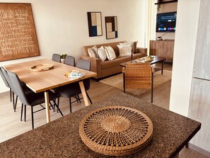 A modern living room with a sofa, dining table, and chairs. There is a TV mounted on the wall and a decorative wall piece. - Duplex House Pool and Beaches Nearby (Bávaro)