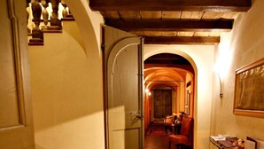 Un couloir étroit doté d’un sol carrelé, d’un escalier en bois et d’une porte donnant sur une pièce où se trouvent un buffet rouge et un miroir.