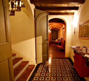 A narrow hallway with a tiled floor, a wooden staircase, and a door leading to a room with a red cabinet and a mirror. - La Locanda Di Bagnara (Bagnara di Romagna)